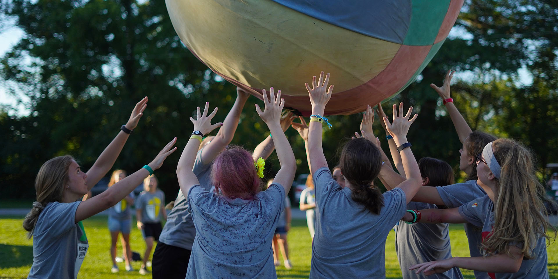 A group of campers are reaching upwards toward a large colorful ball.