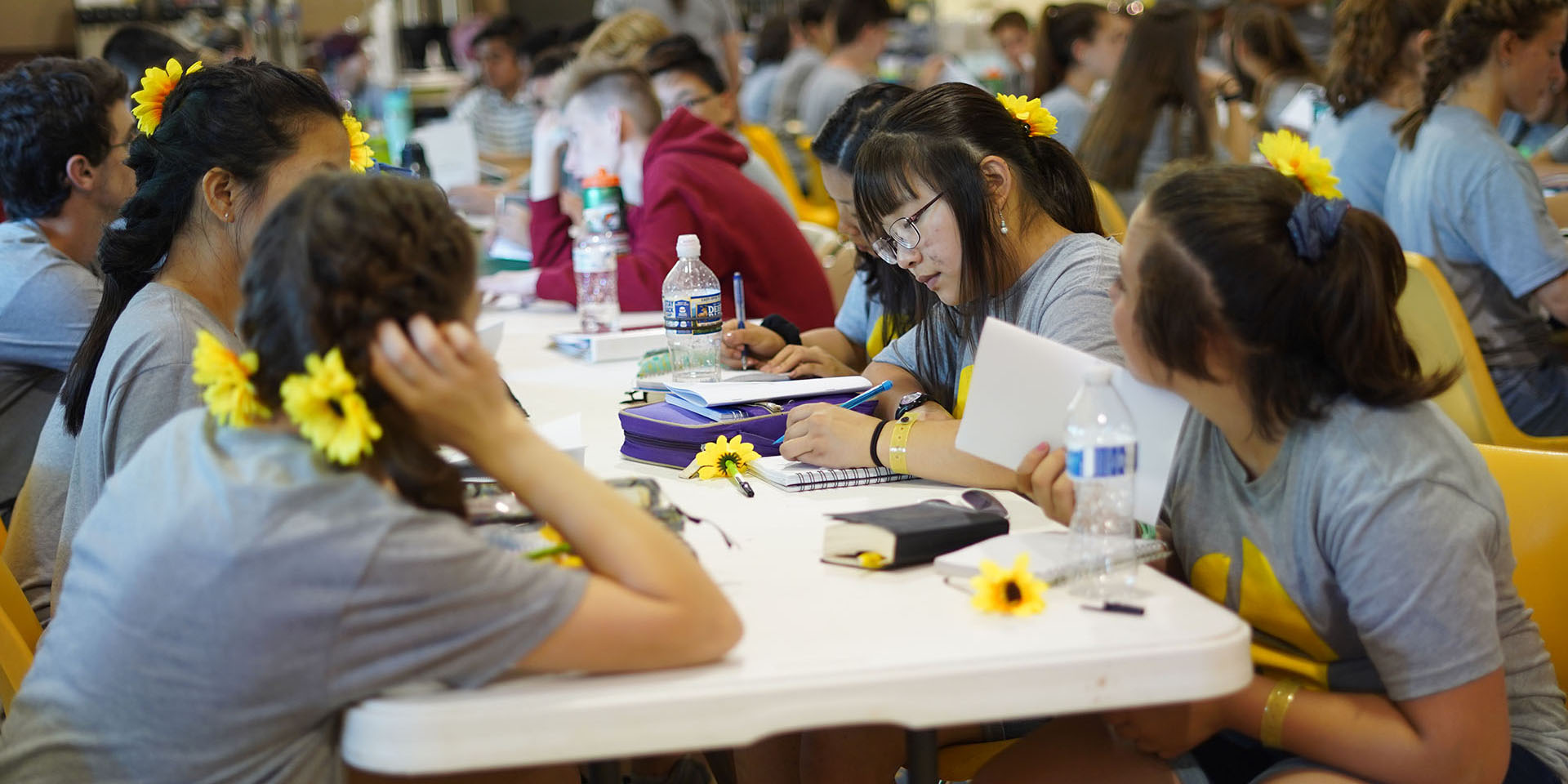 A group of campers sit at a table with bibles and notebooks.